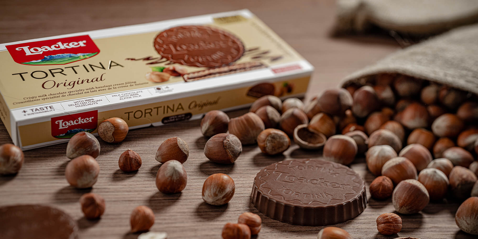 Loacker Tortina Original with unwrapped Tortina and hazelnut scattered around on wooden table