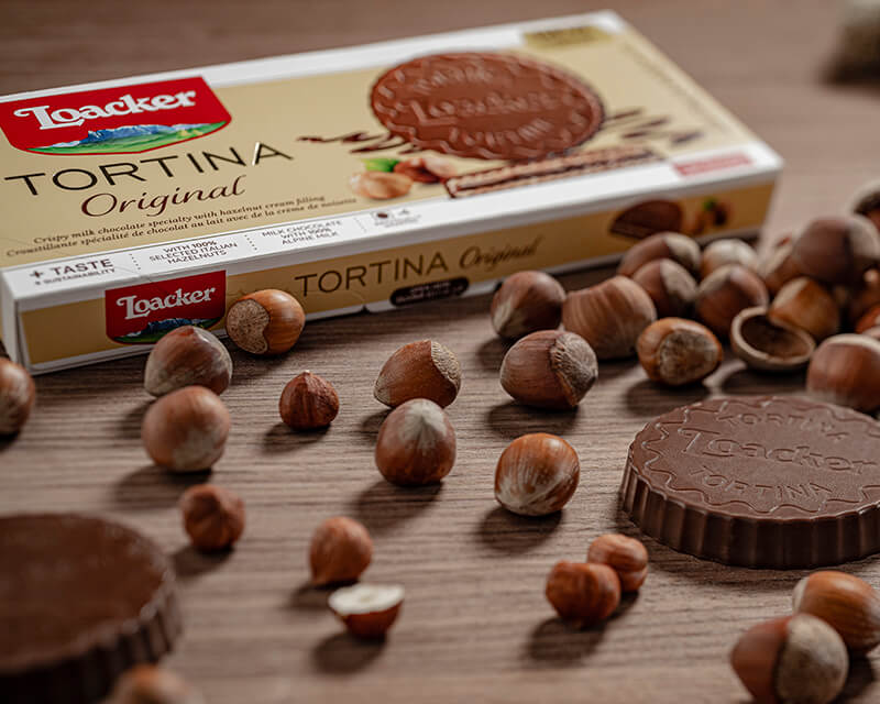 Loacker Tortina Original with unwrapped Tortina and hazelnut scattered around on wooden table