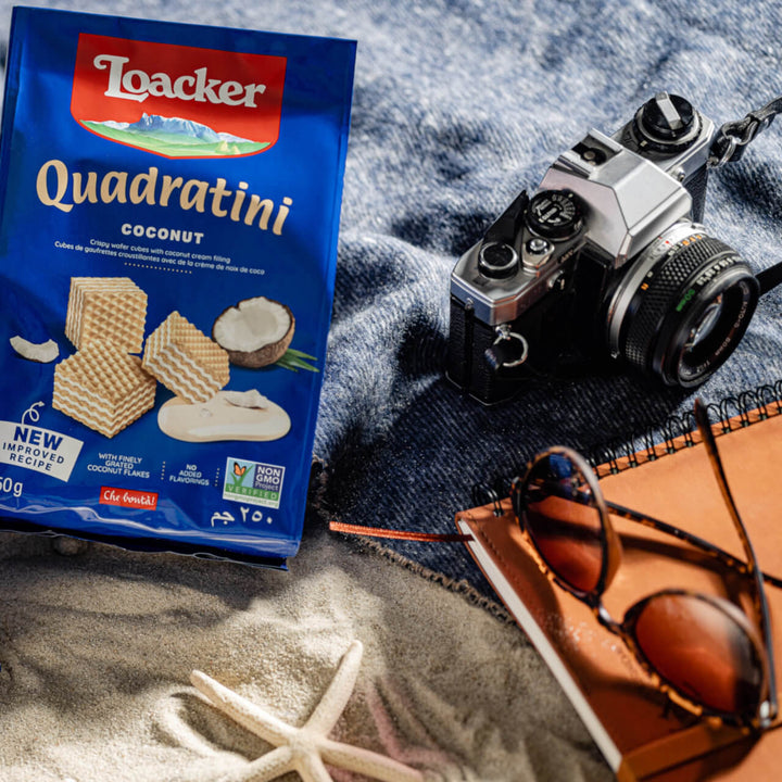 Quadratini Coconut, Creme-Filled Wafer Cookies, 8.82 oz. Bag with camera, glasses and note book next to it on a beach