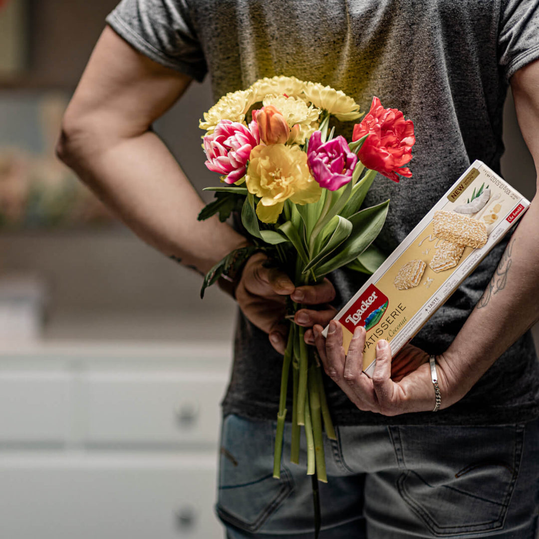 Men holding Patisserie White Coconut, Chocolate Coated Specialty, 3.53 oz. Box with bouquet flowers.